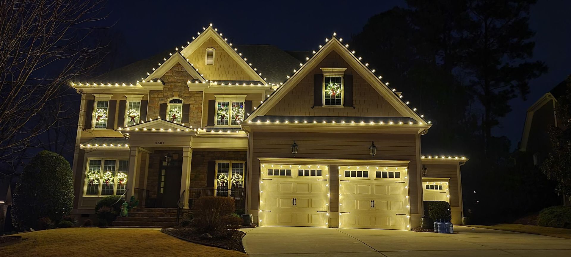 Well-lit two-story suburban house at night with holiday lights along the roofline and windows.