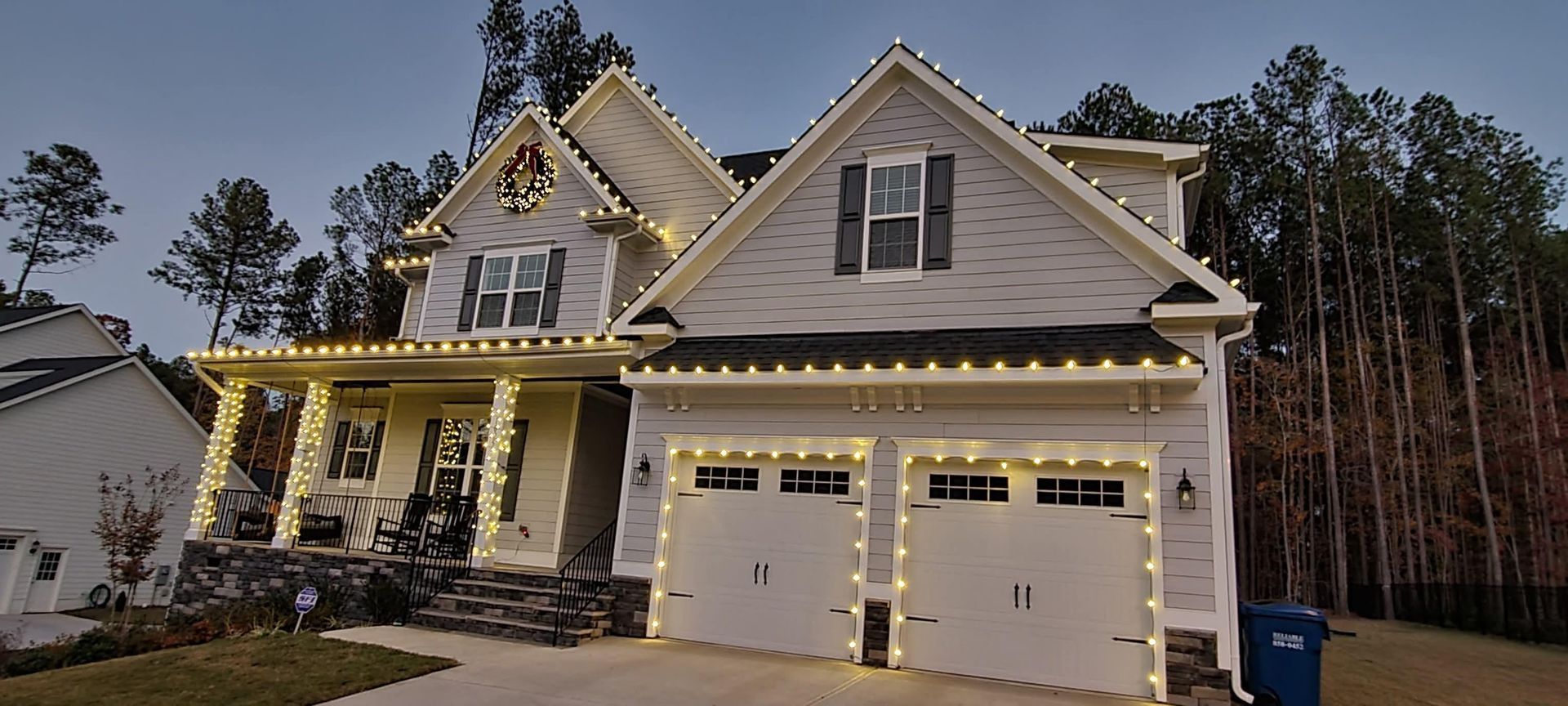 Two-story suburban house with lit porch, double garage, and dusk sky