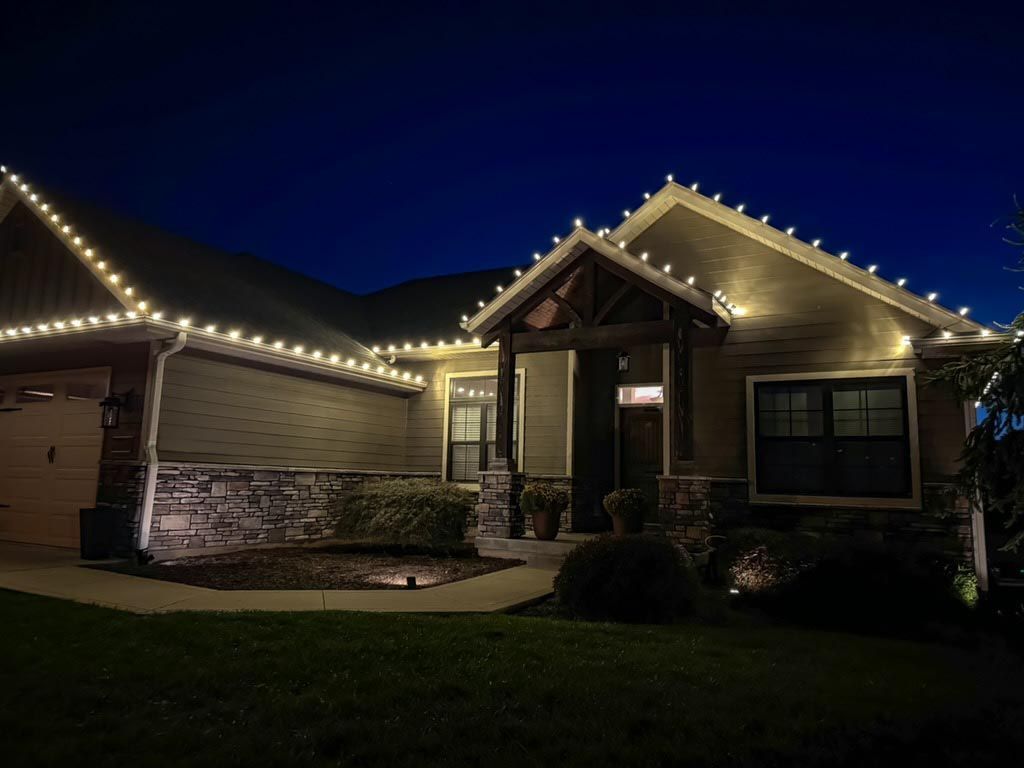 House at night with warm white string lights outlining the roof and porch.