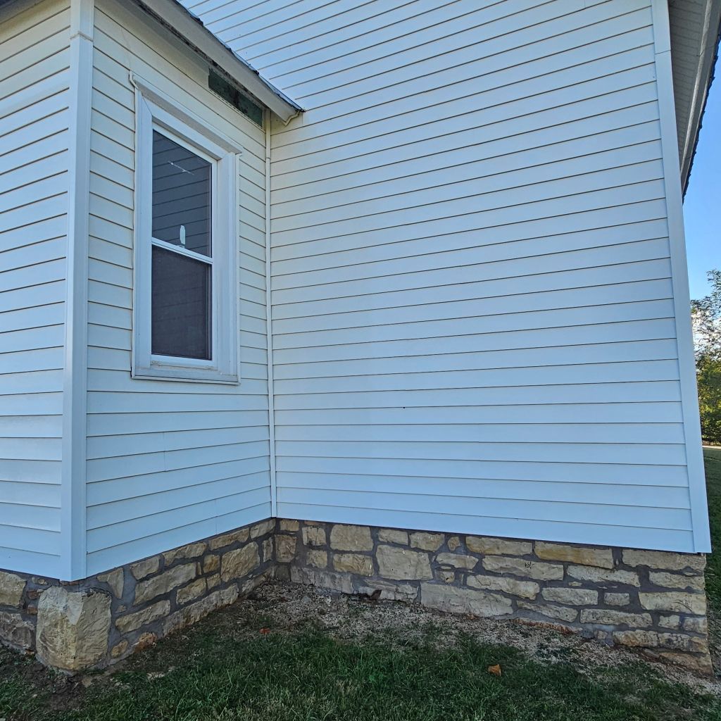White house siding with a stone foundation and a small window corner.