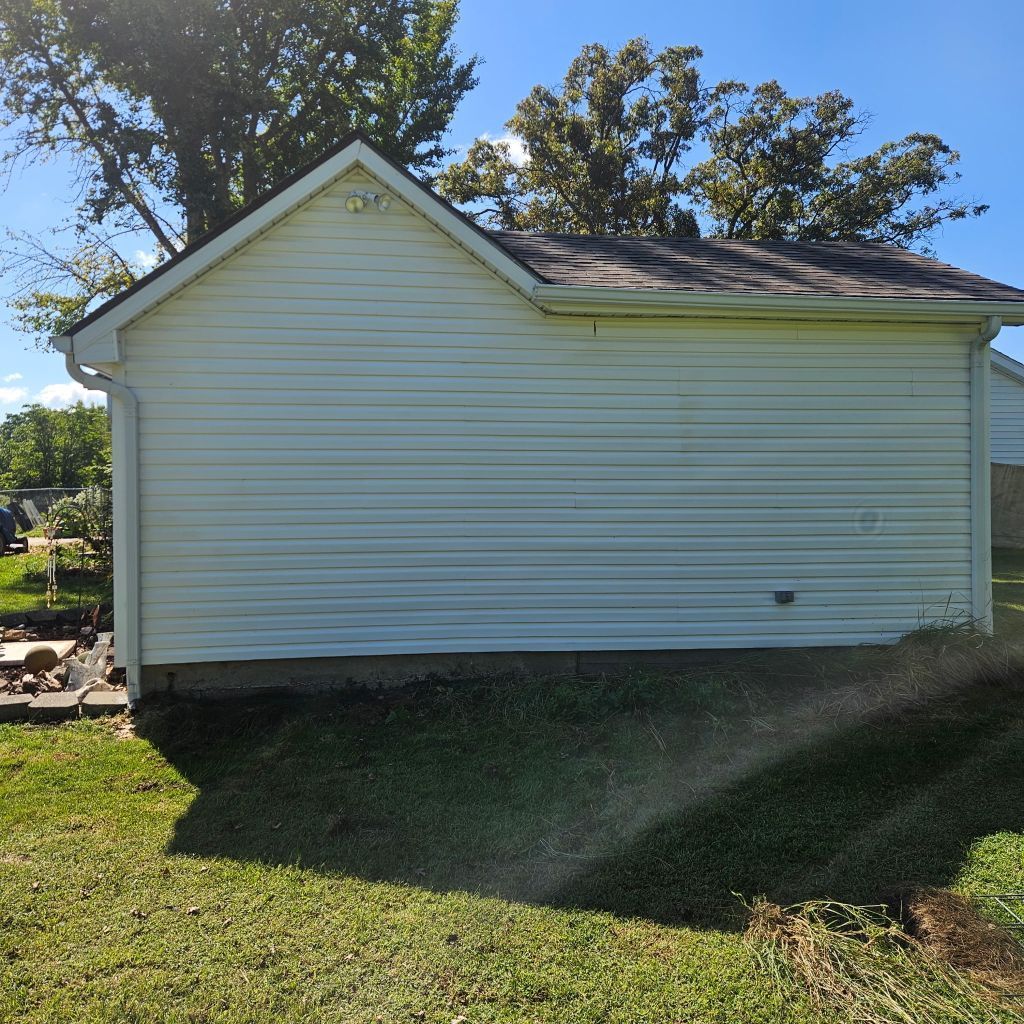 White single-story house exterior with blue siding and a gabled roof in a sunny yard.