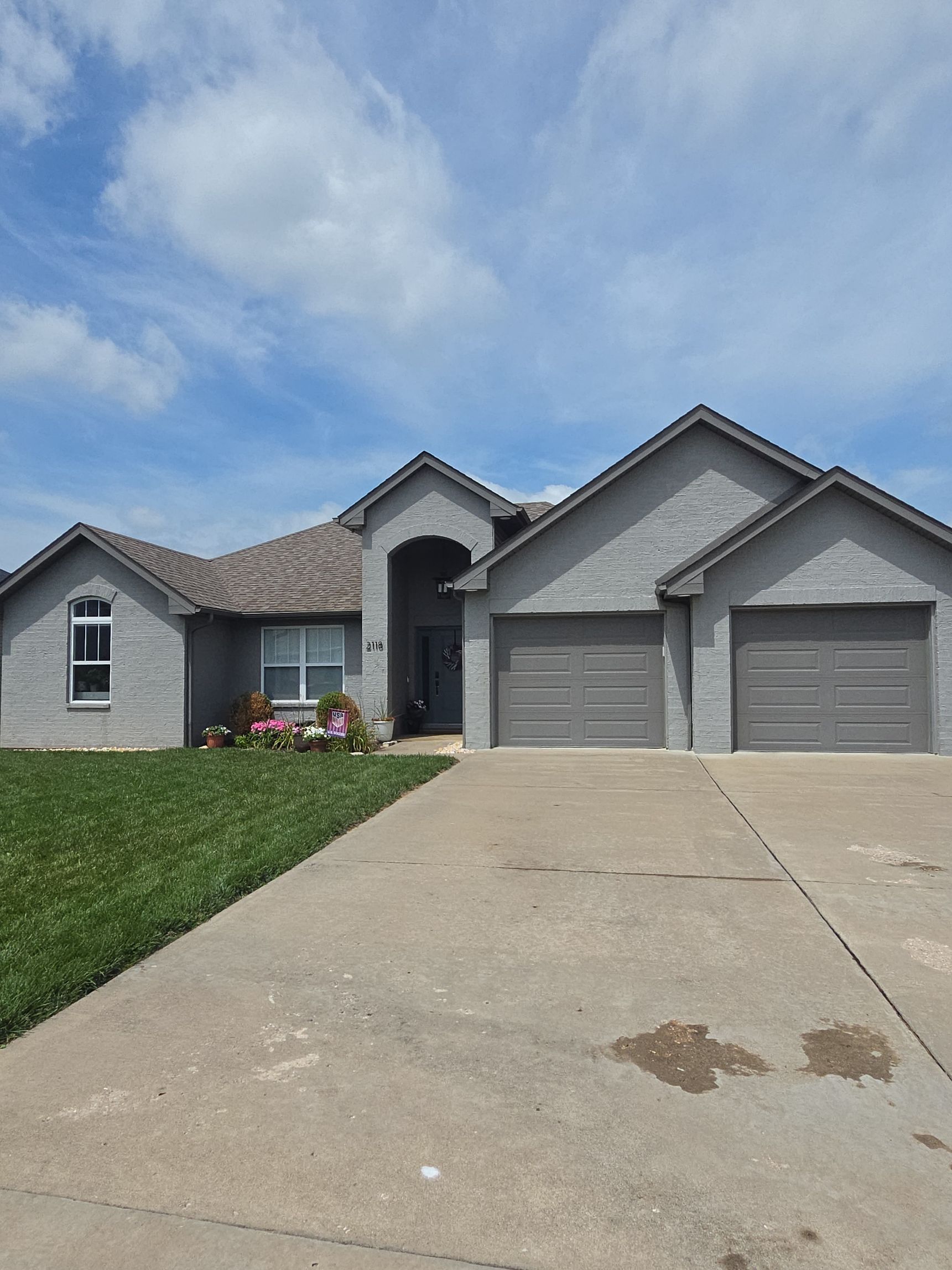 Suburban house with gray siding, two-car garage, and a sloped concrete driveway under a partly cloudy sky