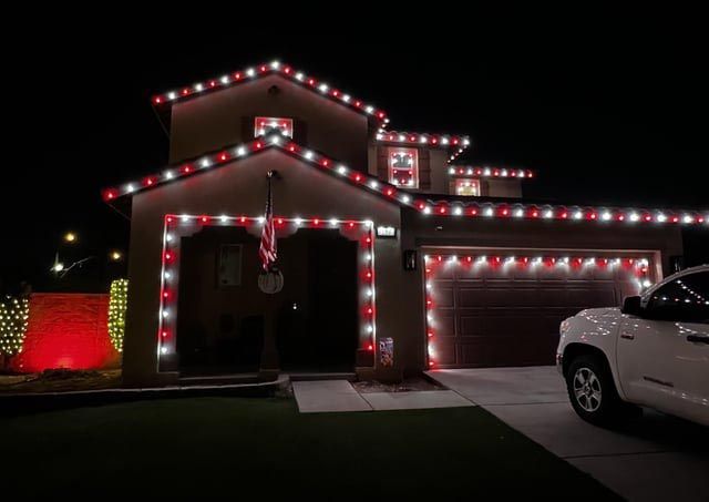 House outlined with red and white Christmas lights at night, with a white SUV parked in the driveway.