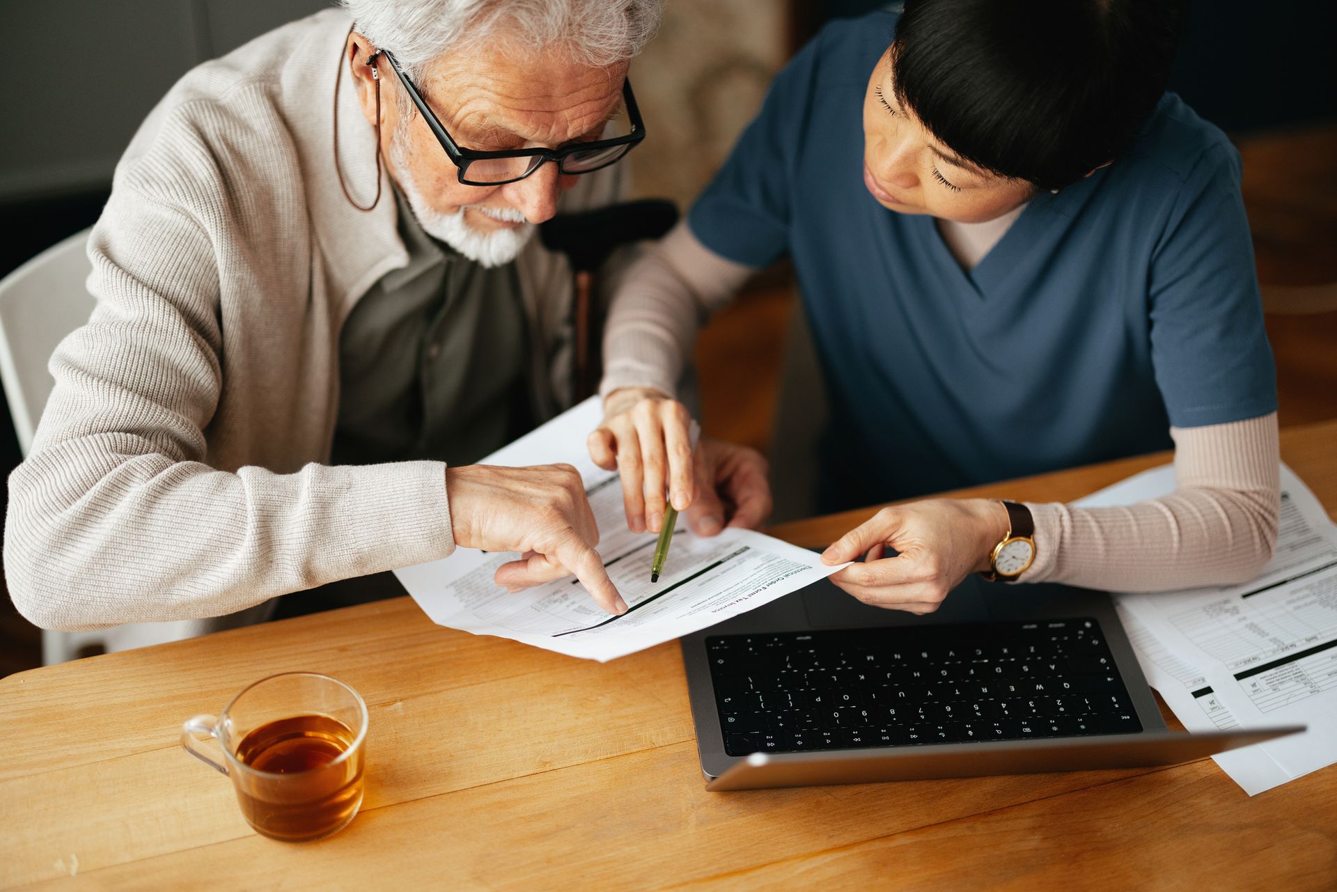 An elderly man and a nurse are looking at a laptop computer.