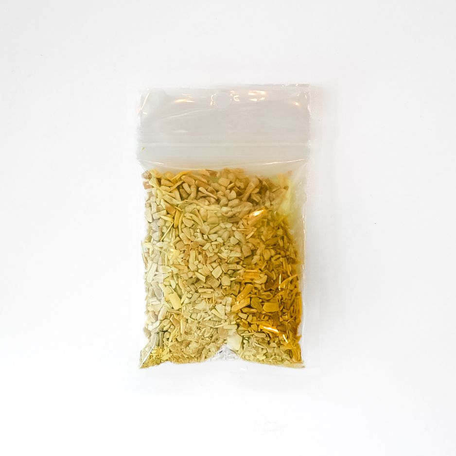 Small clear plastic bag with a bright yellow label, partly filled with dried plant pieces on a white background.