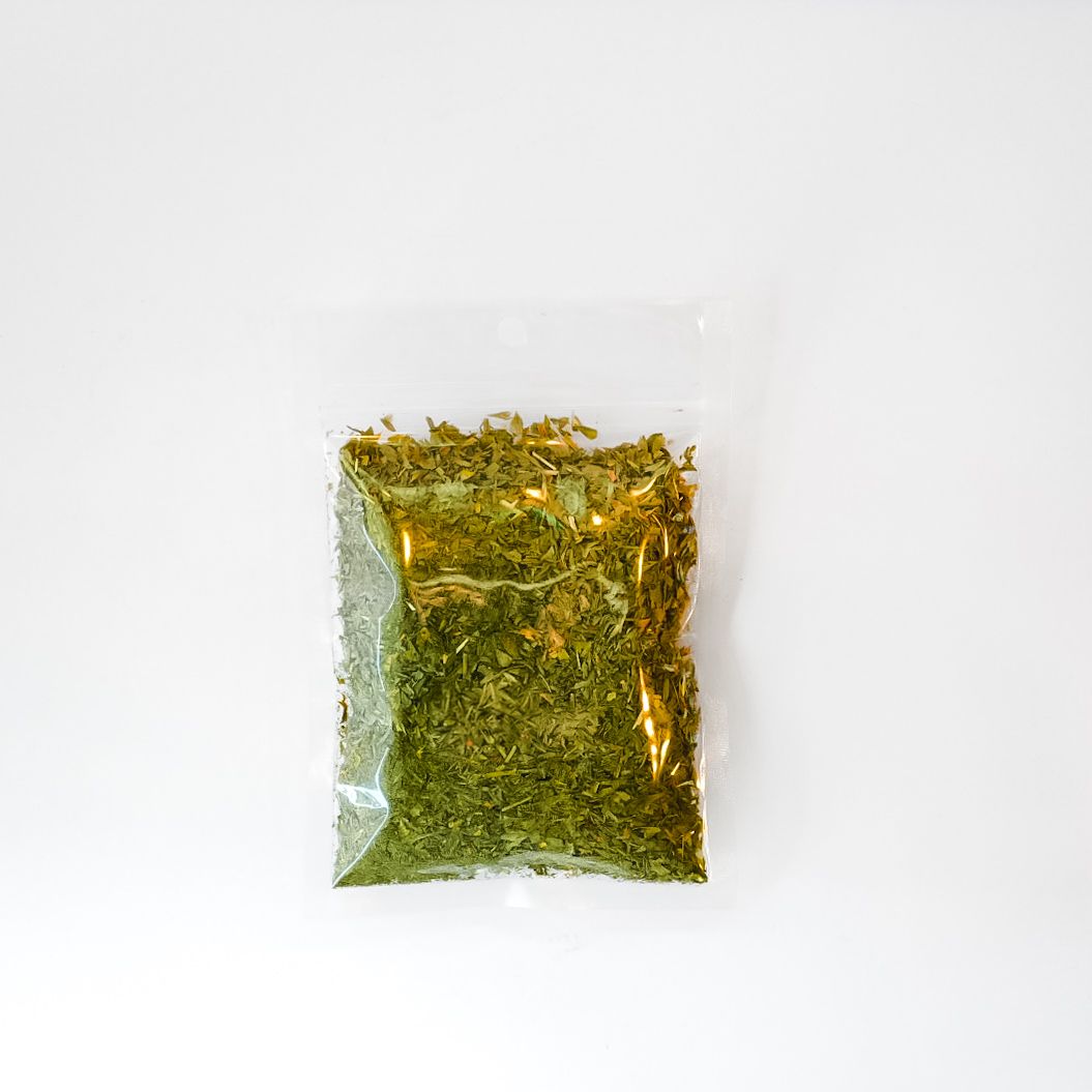 Small clear plastic bag of dried green herbs with a bright yellow label on a white background