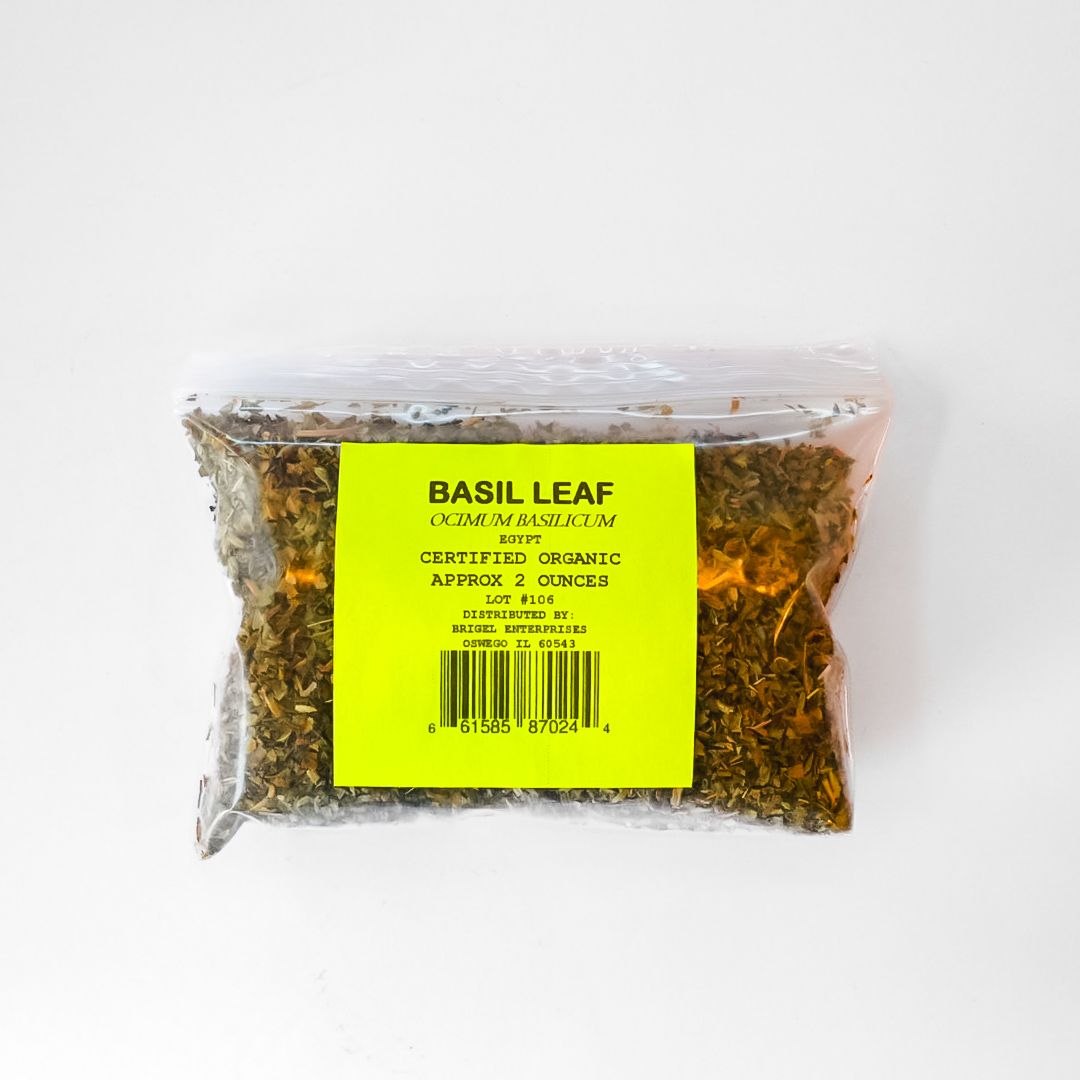 Clear plastic bag of dried basil leaves with a bright yellow label and barcode on a white background
