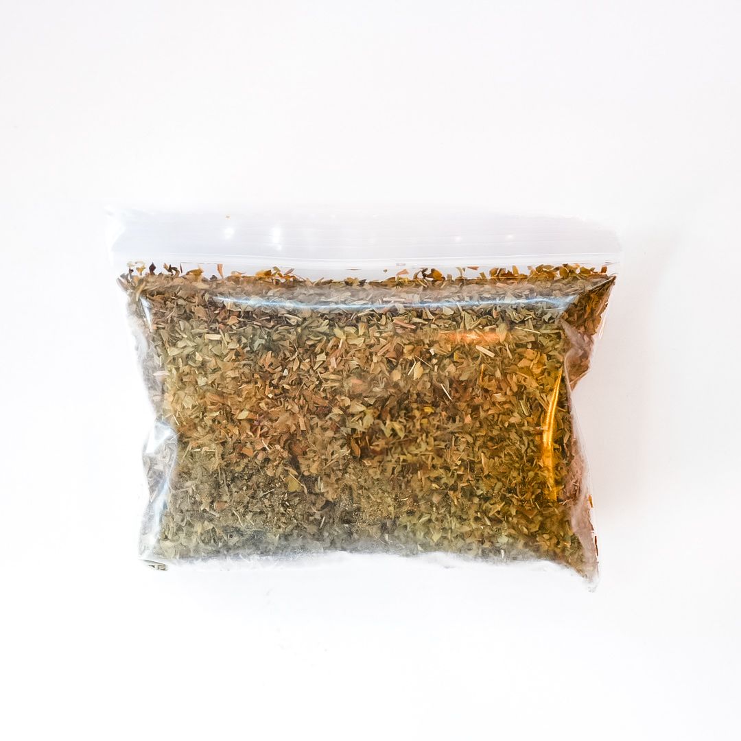 Clear plastic bag of dried basil leaves with a bright yellow label and barcode on a white background
