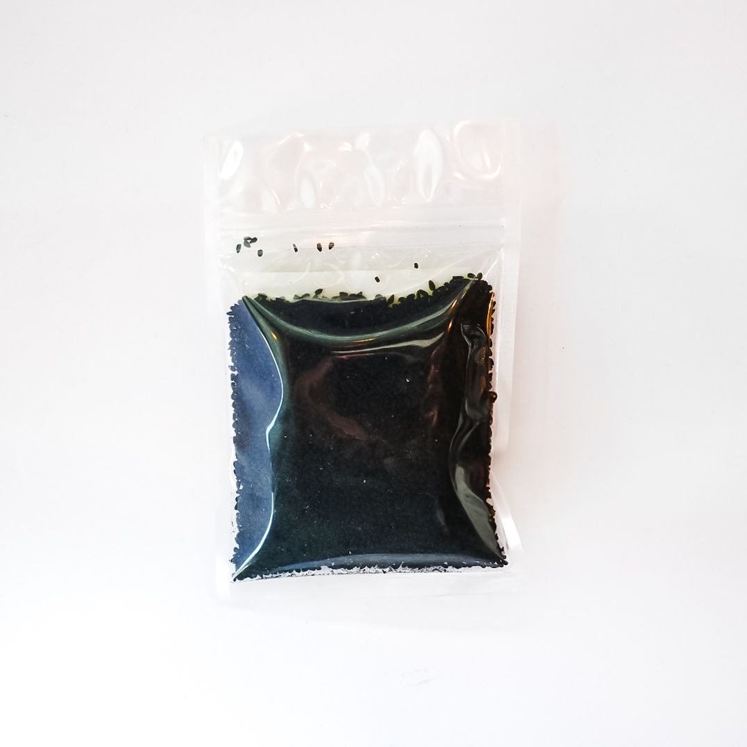 Small clear plastic bag of black seeds with a bright yellow label on a white background