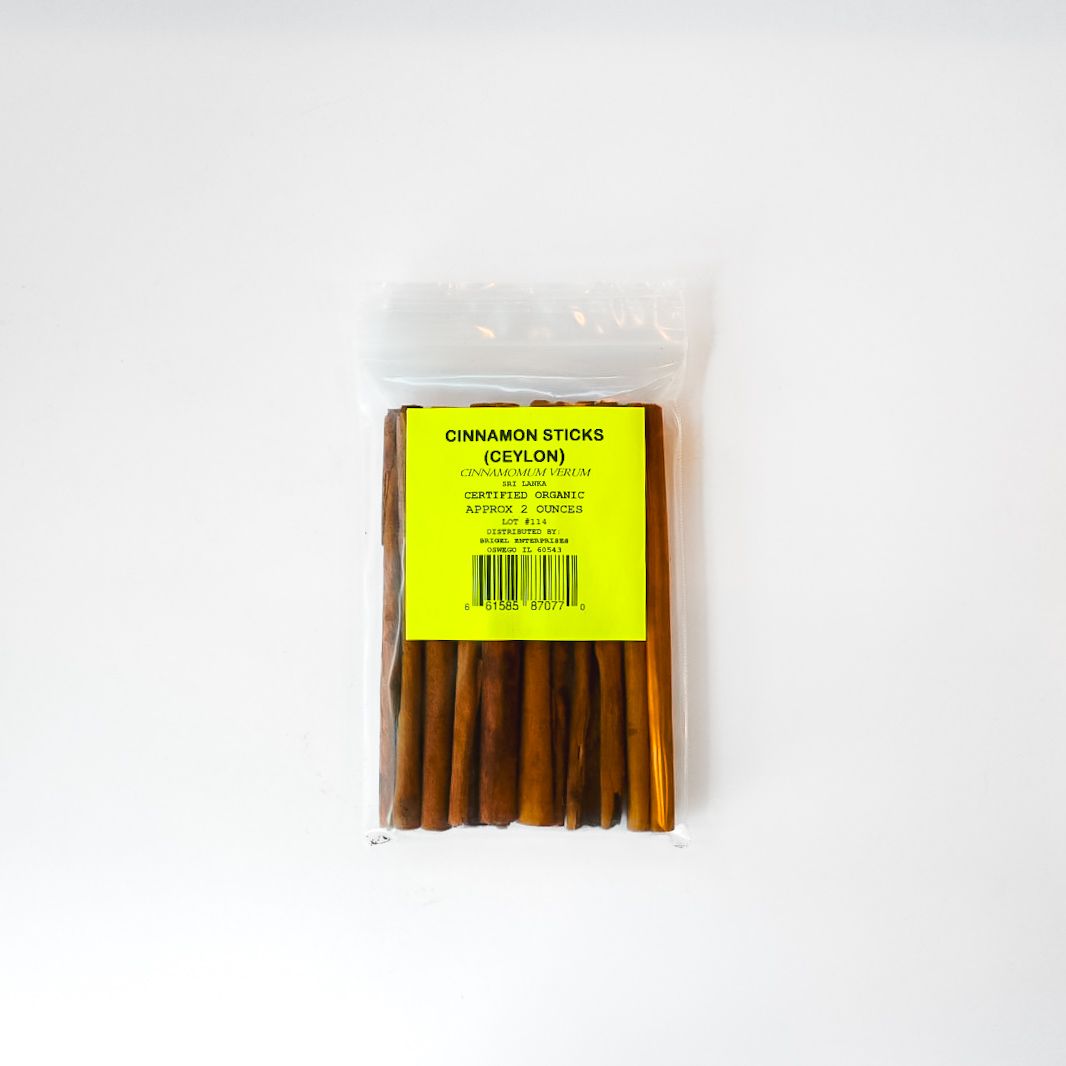 Clear plastic bag of brown cinnamon sticks with a bright yellow label on a white background