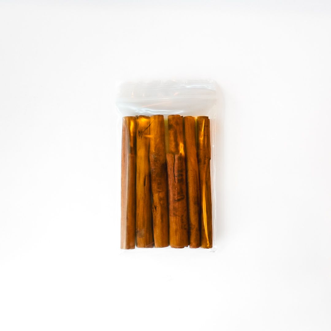 Clear plastic bag of brown cinnamon sticks with a bright yellow label on a white background