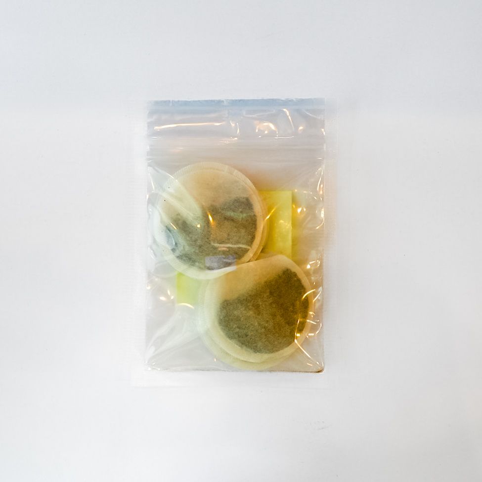 Clear plastic bag with a yellow label holding a round container on a white background