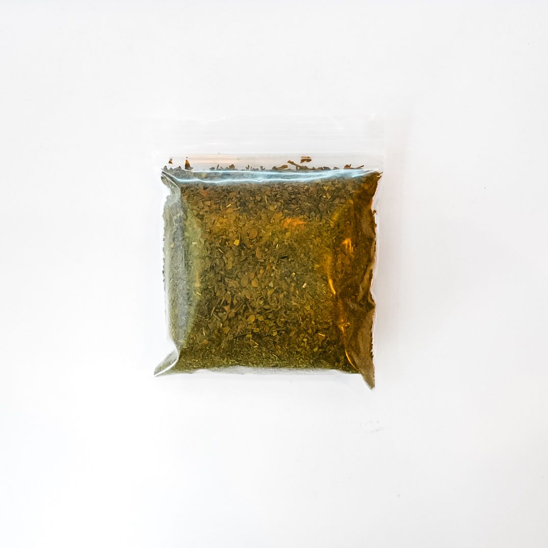 Clear plastic bag of dried chaparral leaf tea with a bright yellow label on a white background