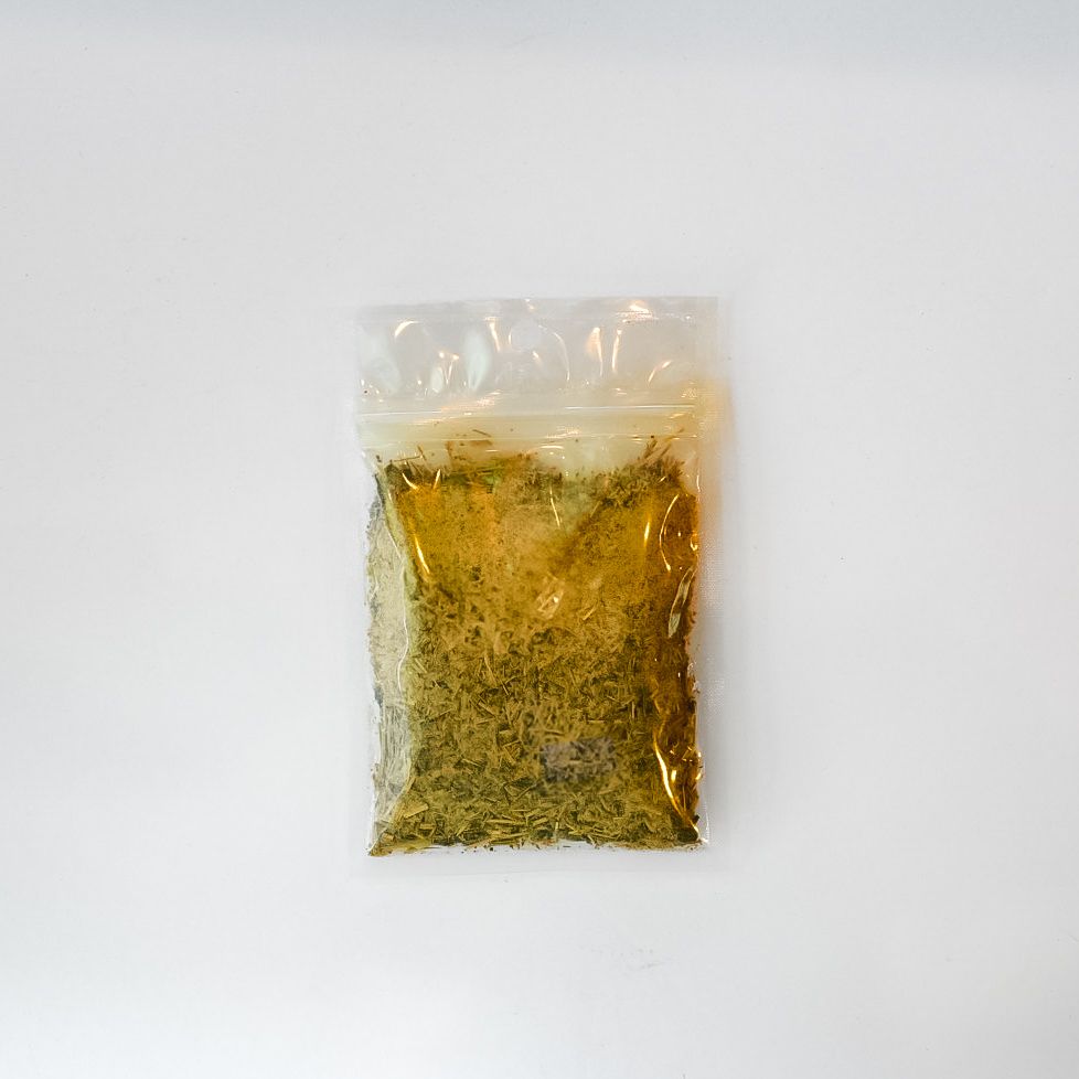 Small clear plastic bag of dried herbal blend with bright yellow label on a white background
