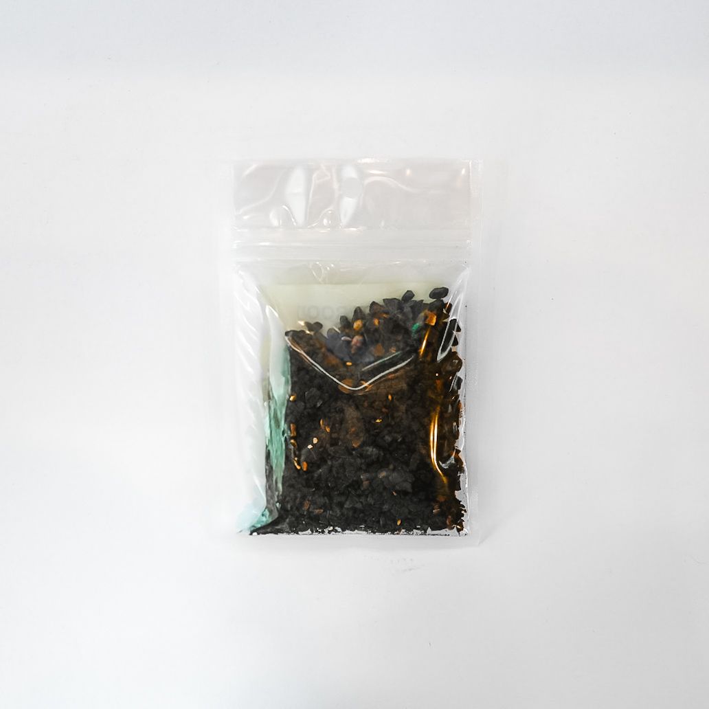 Small clear plastic bag of black material with a bright yellow label on a white background