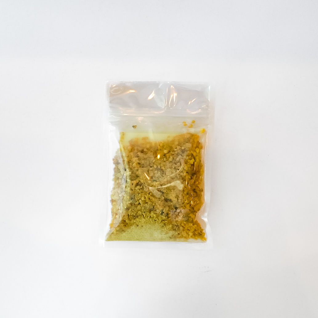 Clear plastic bag of dried yellow plant material with a bright green label on a white background