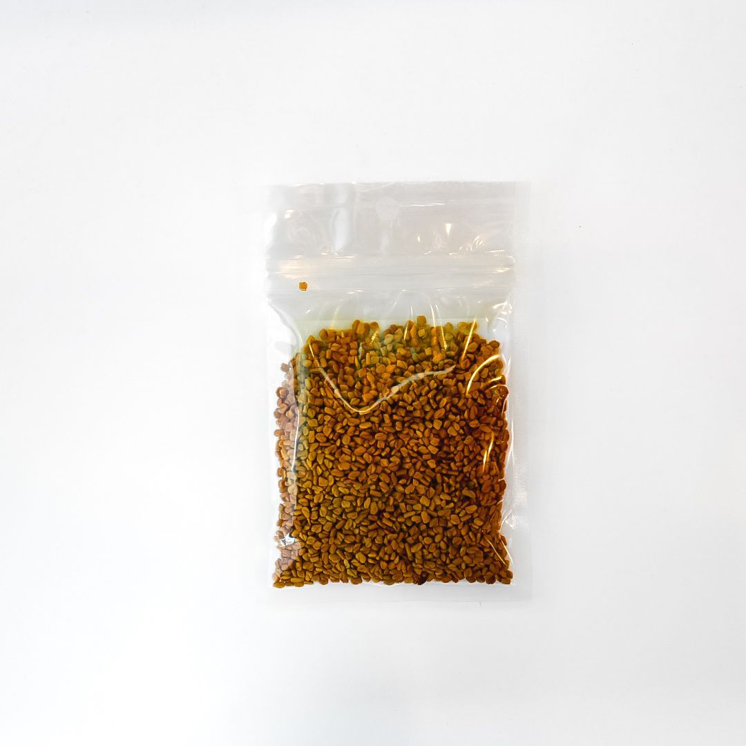 Small clear bag of fenugreek seed with a bright yellow label on a white background