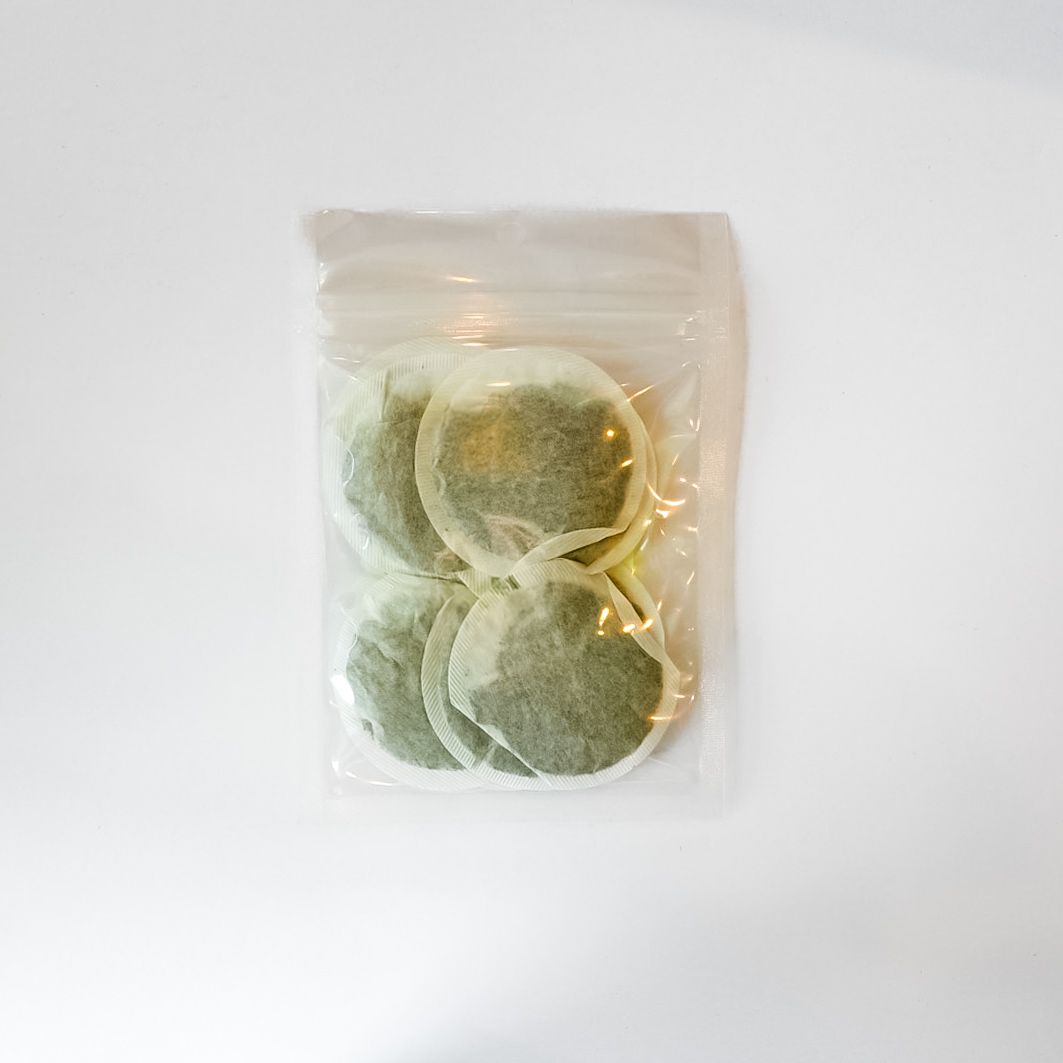 Plastic bag of green tea leaf tea bags with a bright yellow label on a white background
