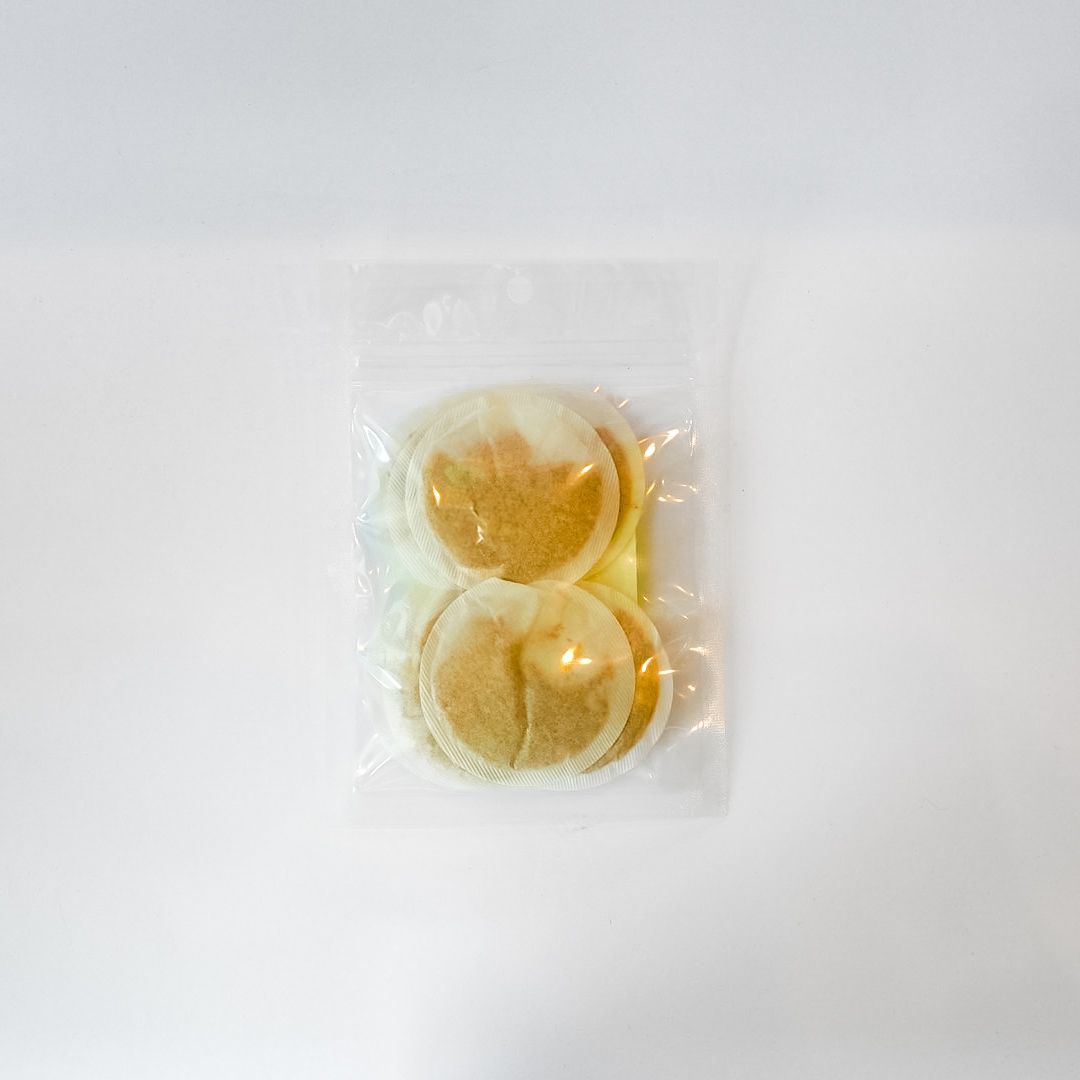 Clear bag of round tan tea bags with a bright yellow label on a white background