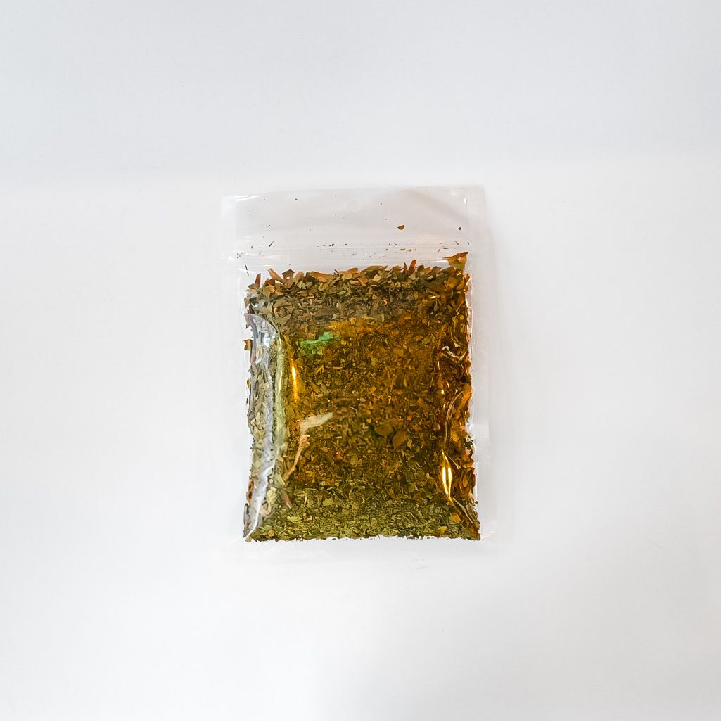 Small clear plastic bag of dried green herb with a bright yellow label on a white background