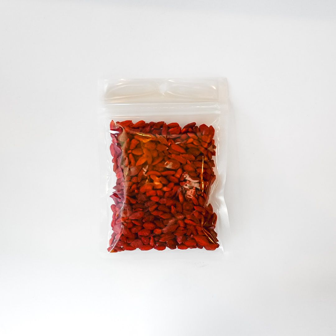 Clear plastic bag of red dried berries with a bright yellow label on a white background