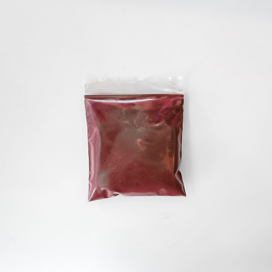 Clear plastic bag of maroon powder with a bright yellow label on a white background