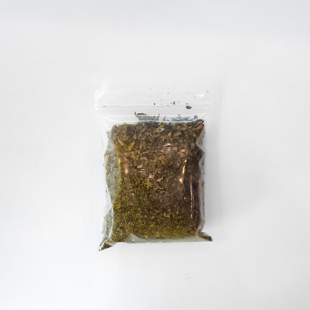 Clear plastic bag of dried holy basil with a bright yellow label on a white background