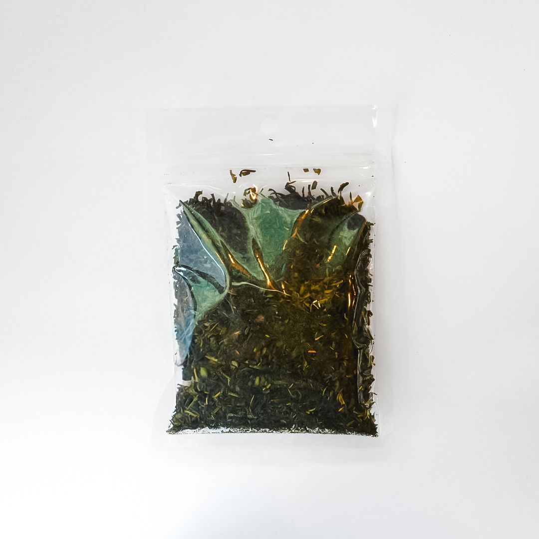 Small clear plastic bag of dark loose tea with a bright yellow label on a white background