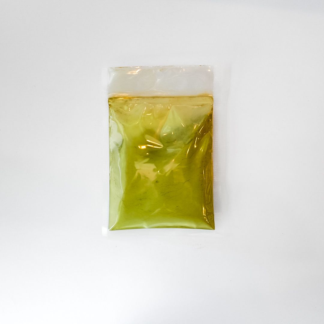 Small clear plastic bag with yellow label and green powder inside on a white background