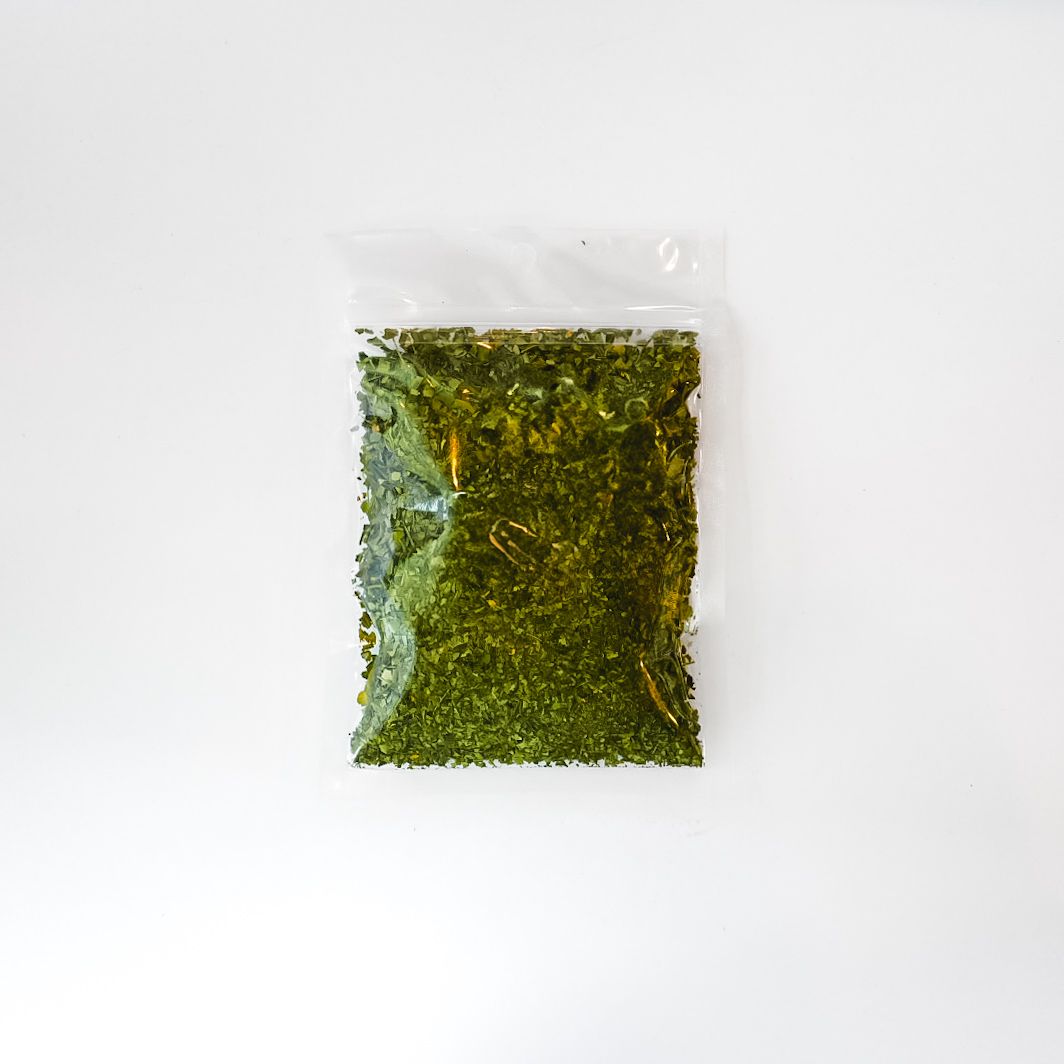 Small clear bag of green herbal material with a bright yellow label on a white background