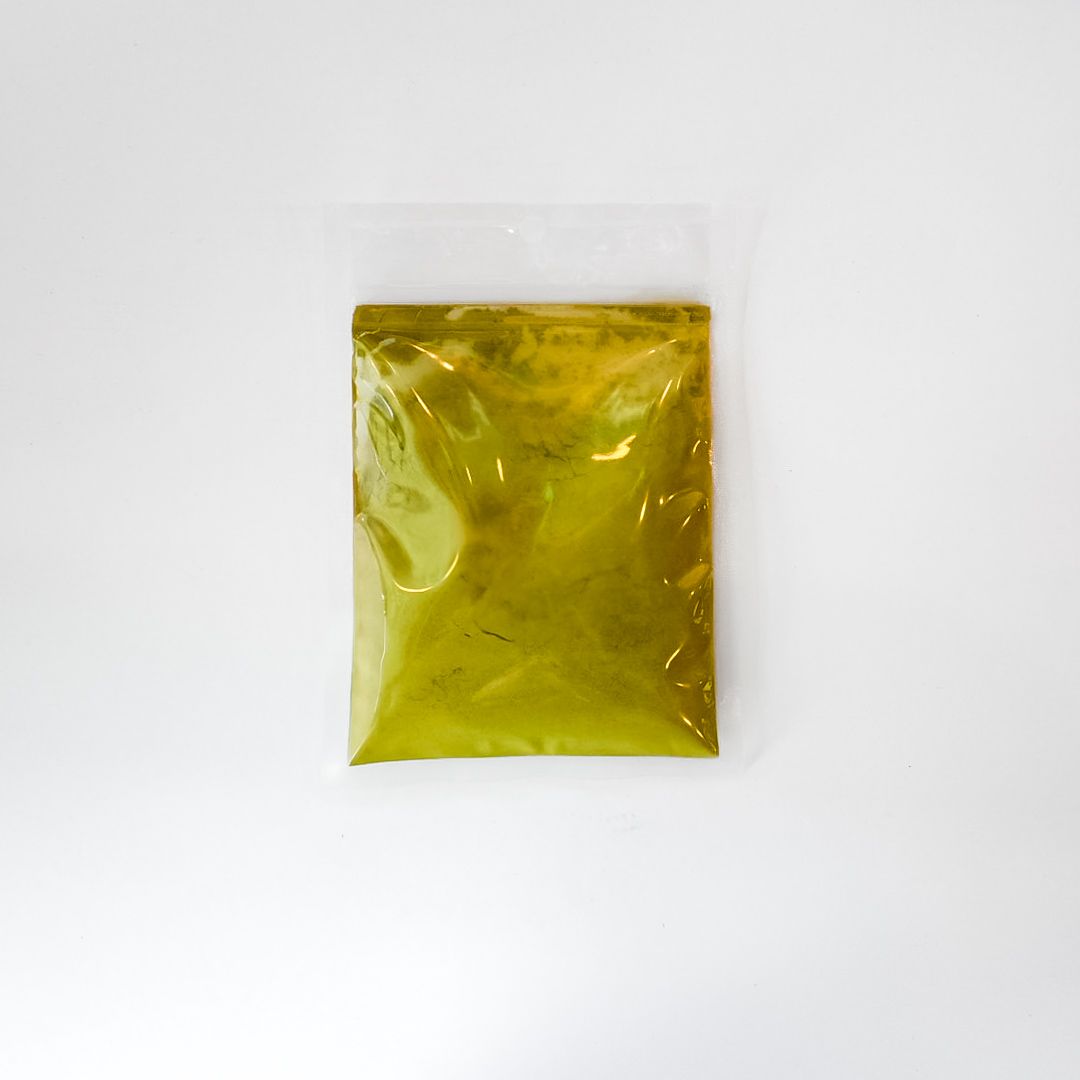 Small clear plastic pouch with yellow label containing greenish powder on a white background