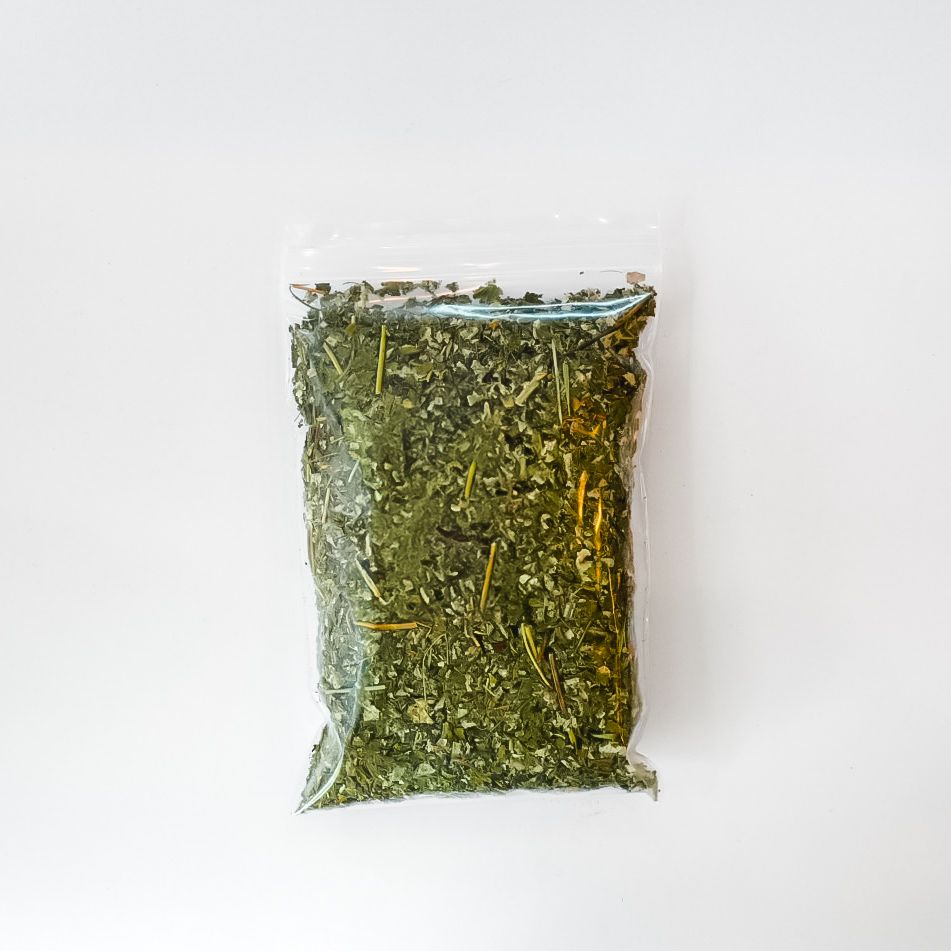 Clear plastic bag of dried green herbs with a bright yellow label on a white background