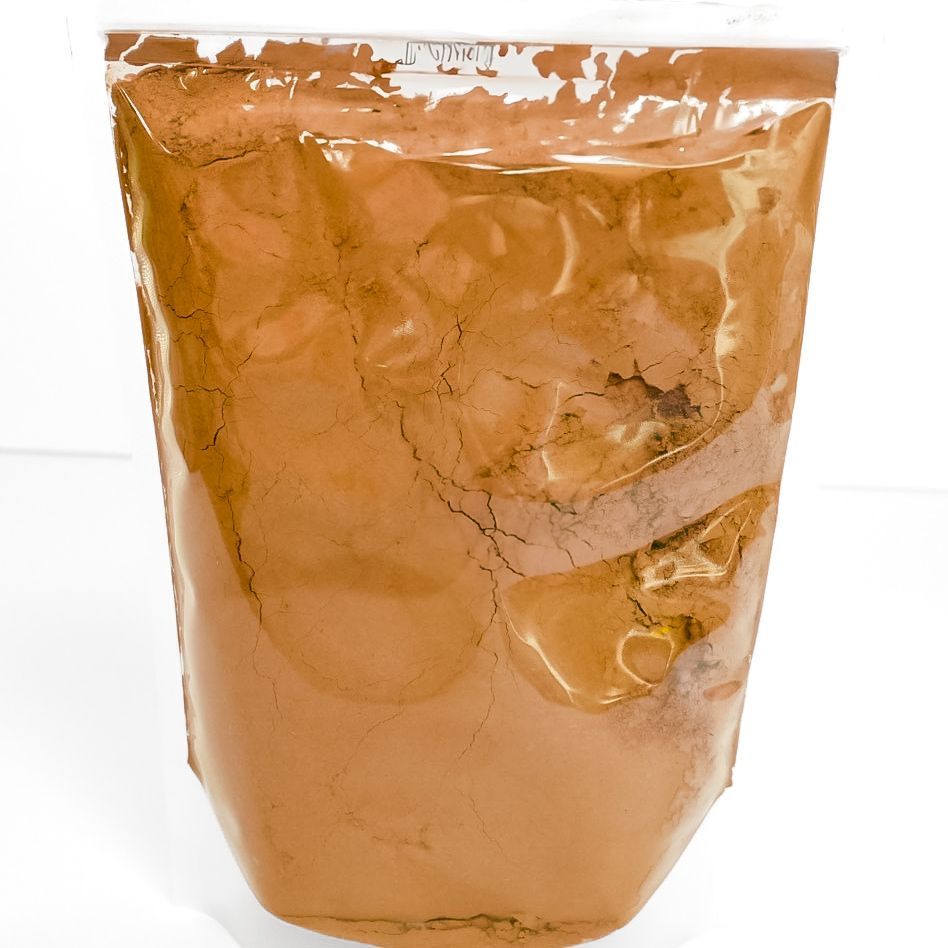 Clear bag of orange-brown powder with a neon yellow label, standing upright on a white surface.