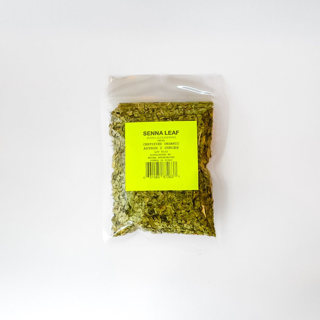 Small clear plastic bag of dried green herbs with a yellow label on a white background