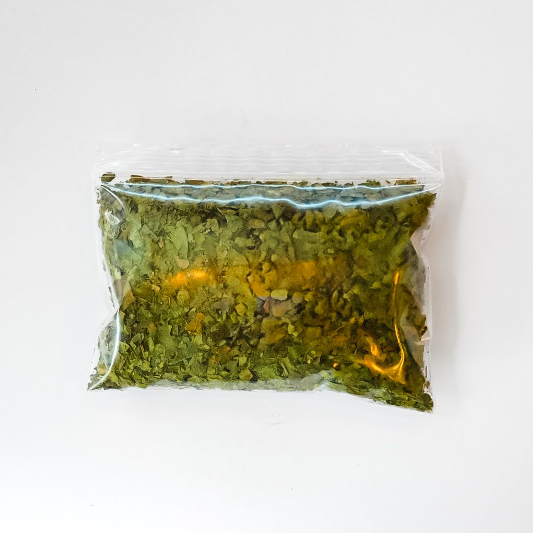 Plastic bag of dried green leaves with a bright yellow label on a white background