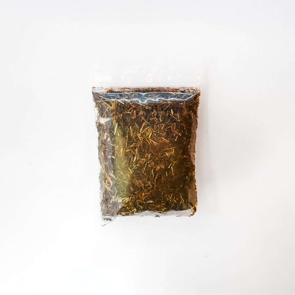 Small clear bag of brown dried herbs with a bright yellow label on a white background