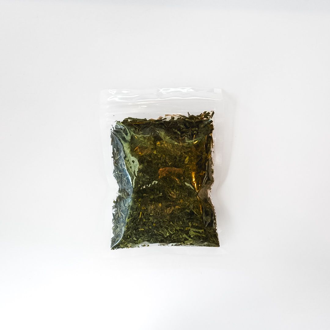 Clear plastic bag of dried tea leaves with a bright yellow label and barcode on a white background