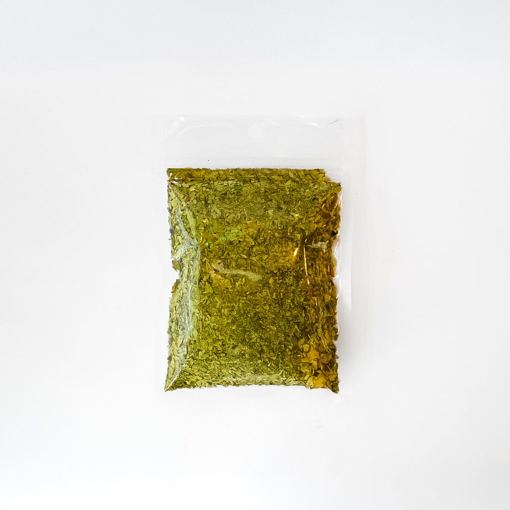 Small clear plastic bag of dried green herbs with a yellow label on a white background