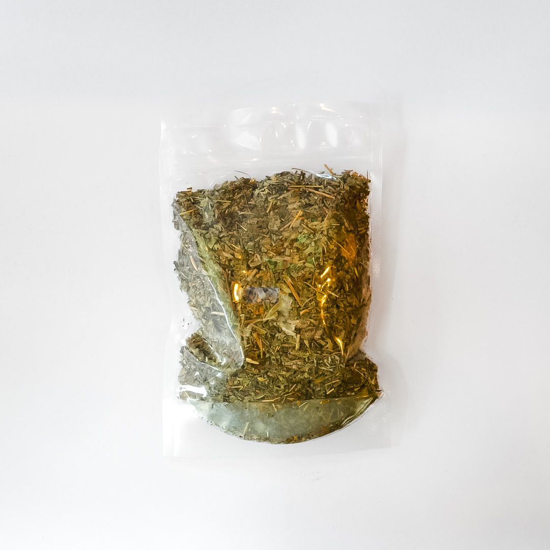 Clear plastic bag of dried herbs or tea with a bright yellow label on a white background