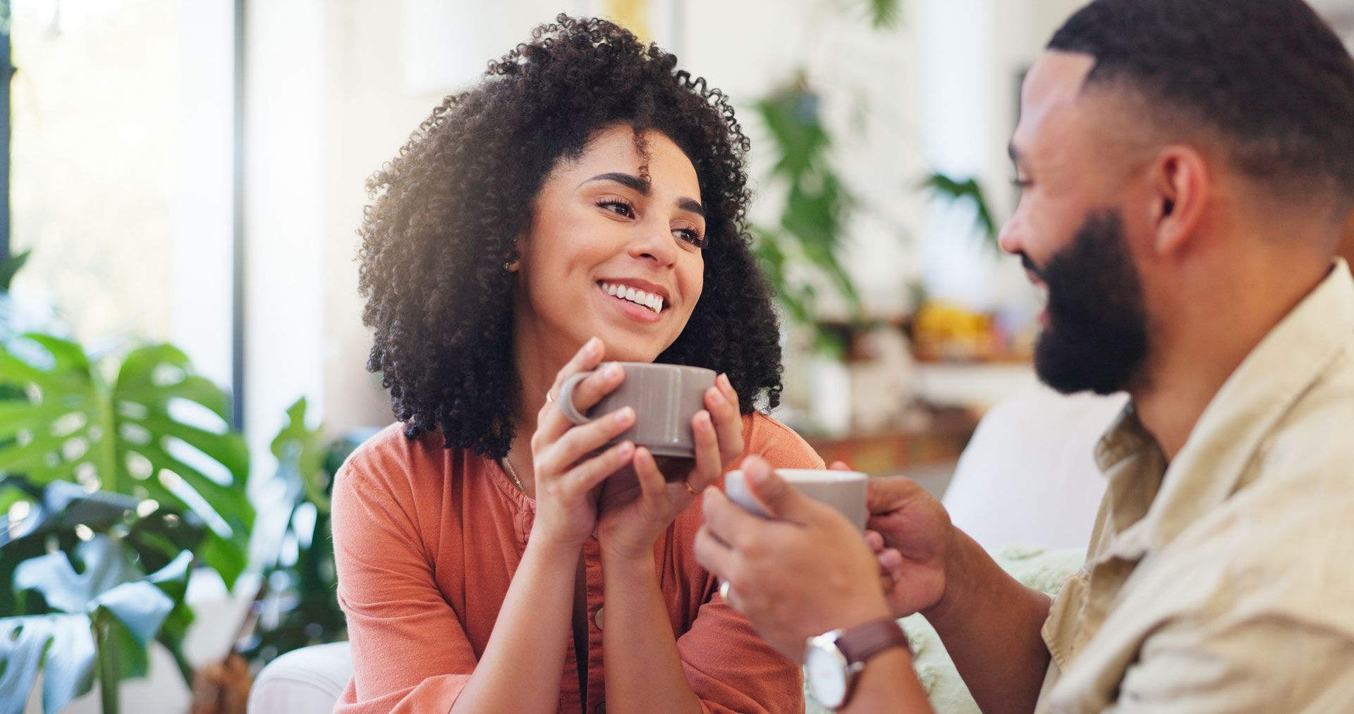 Two people smiling and holding mugs while chatting at a bright cafe table