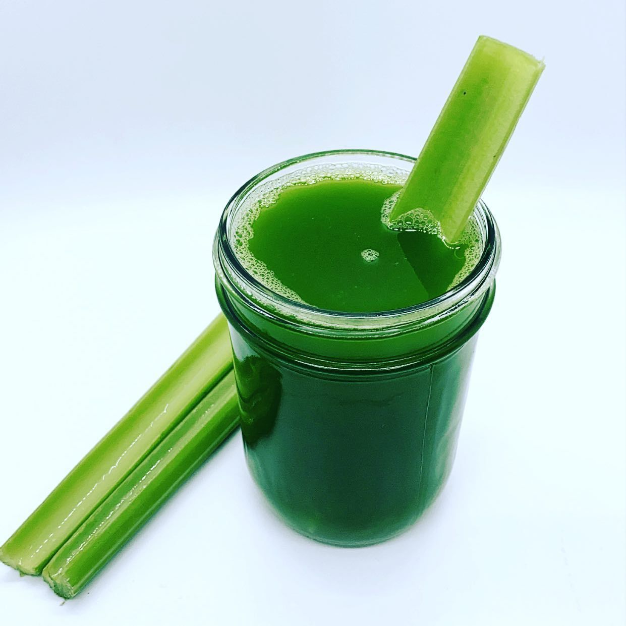 a glass of green juice with celery sticks in it
