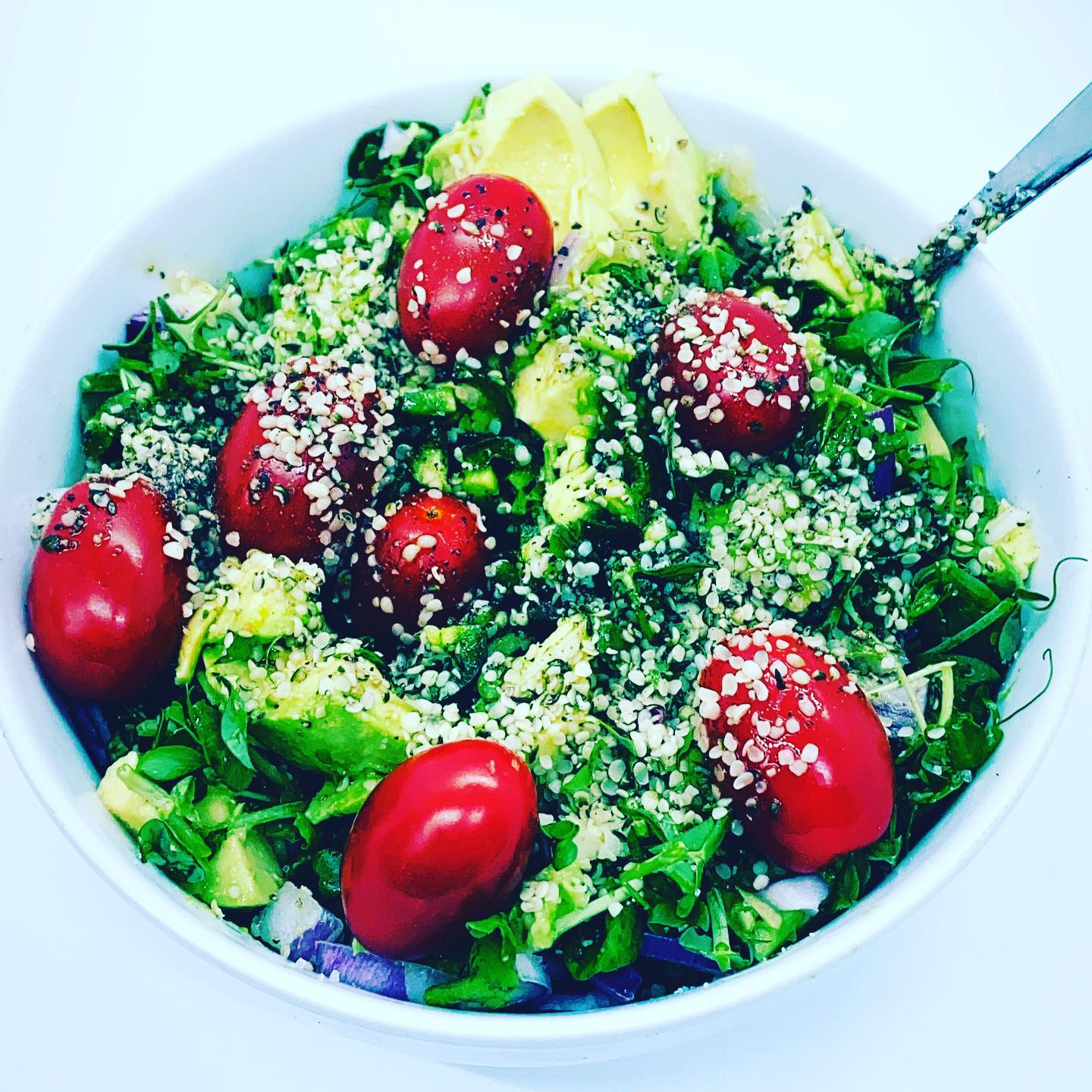 a salad with tomatoes and avocado in a bowl with a spoon