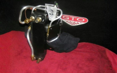 Chrome automotive part with brass fittings on black fabric, beside a red GTO logo patch