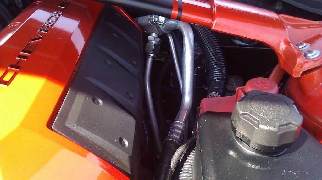 Close-up of red engine bay parts with black hoses and a metal cap, showing a car’s mechanical components.