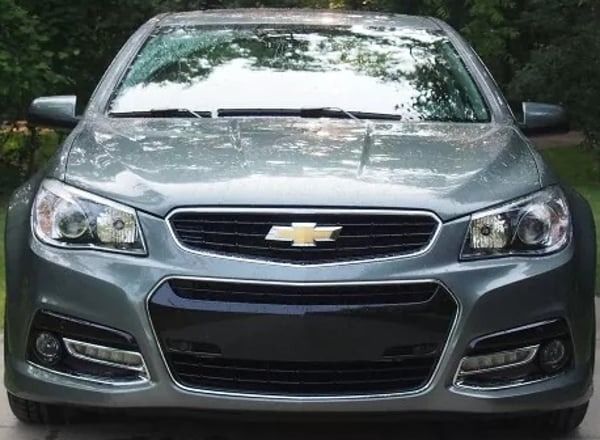 Front view of a gray Chevrolet sedan with headlights on, parked outdoors.