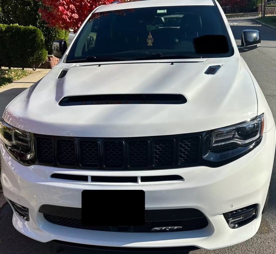 White SUV parked on a sunny residential street, front view with a black grille and hood scoop