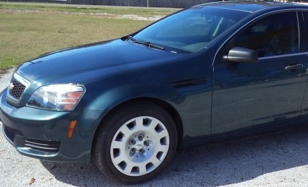 Dark blue sedan parked on a gravel road beside a grassy field