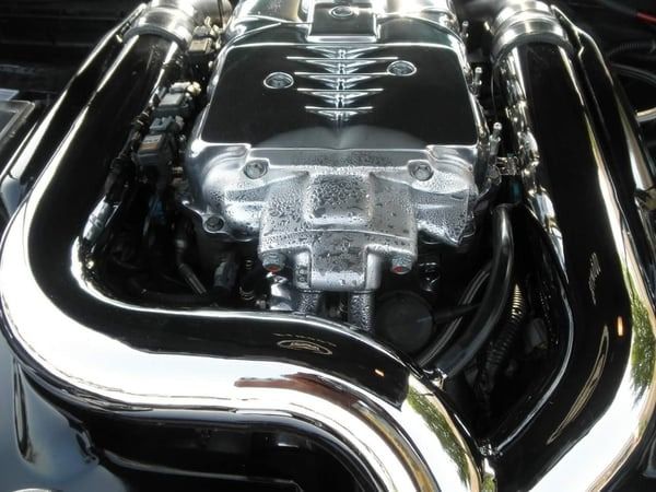 Close-up of a shiny car engine with chrome pipes and a black cover.