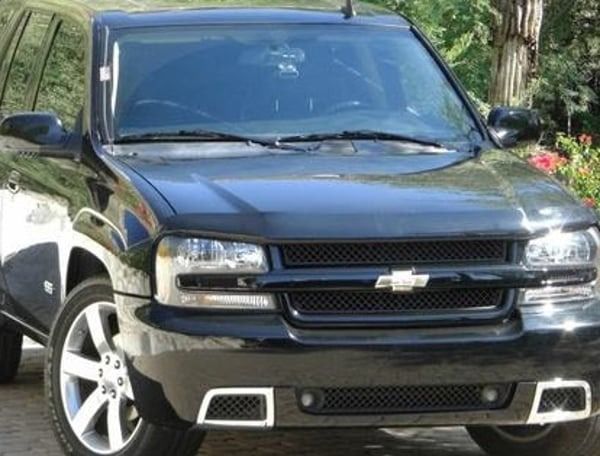 Black Chevrolet SUV parked outdoors in front of trees, viewed from the front-left side