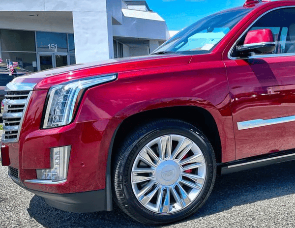 Red Cadillac SUV parked outside a dealership, front side view in bright sunlight